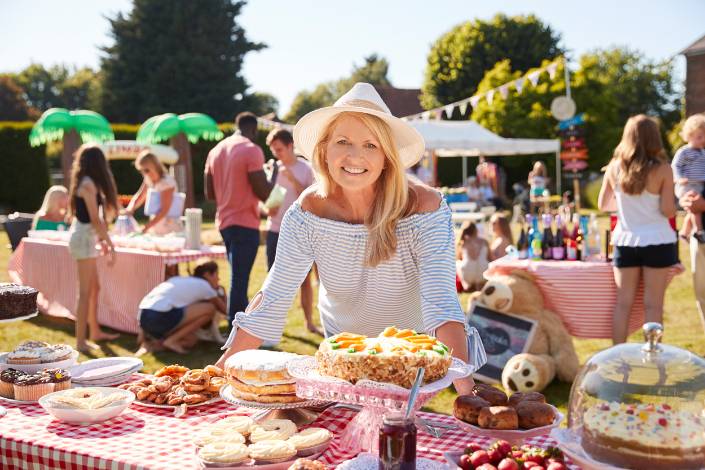 House sitter wearing a hat leaning over a market stall table full of cakes and baked goods